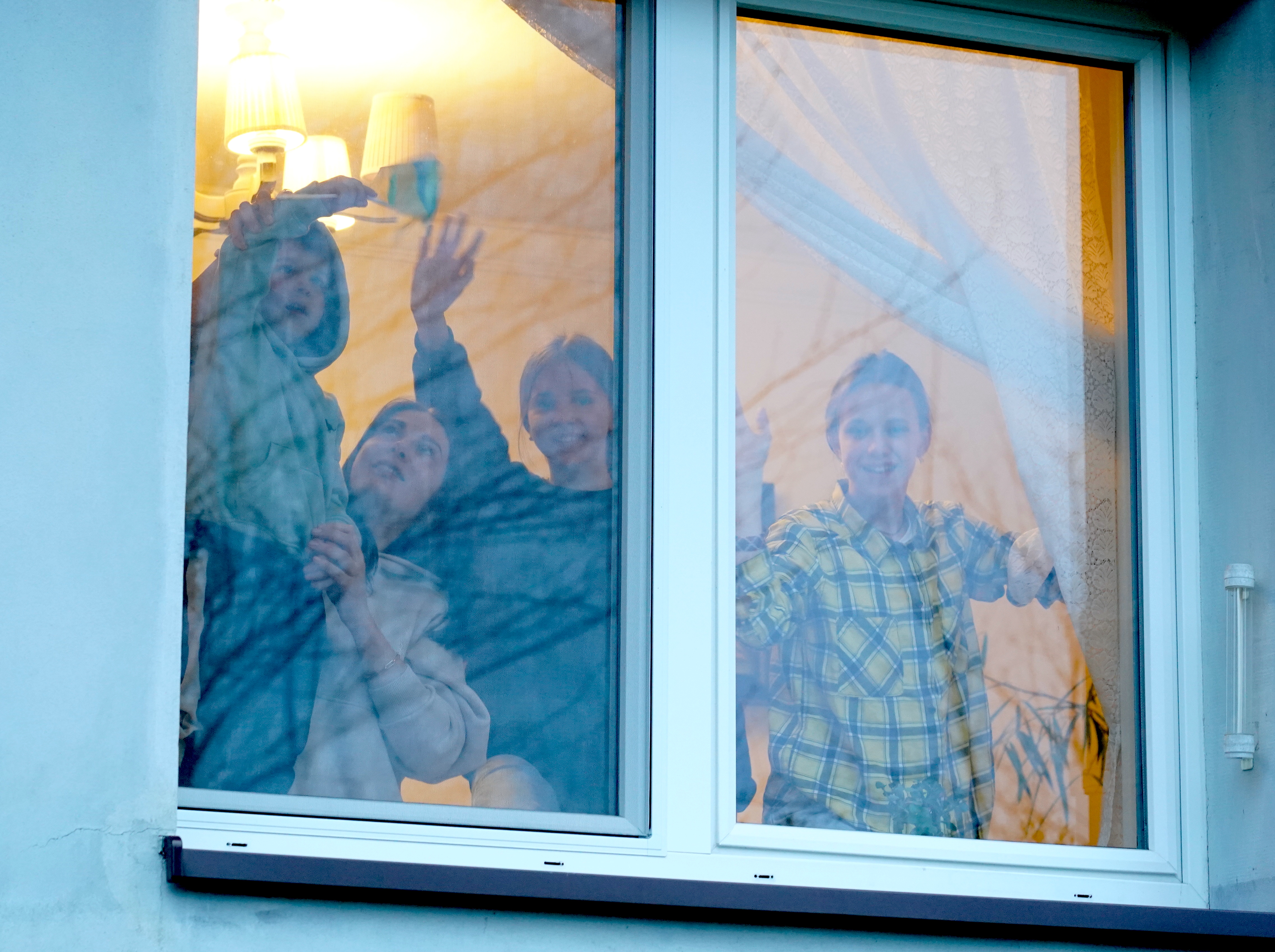 Ukrainian refugees waving from a window of the Polish house where they were welcomed