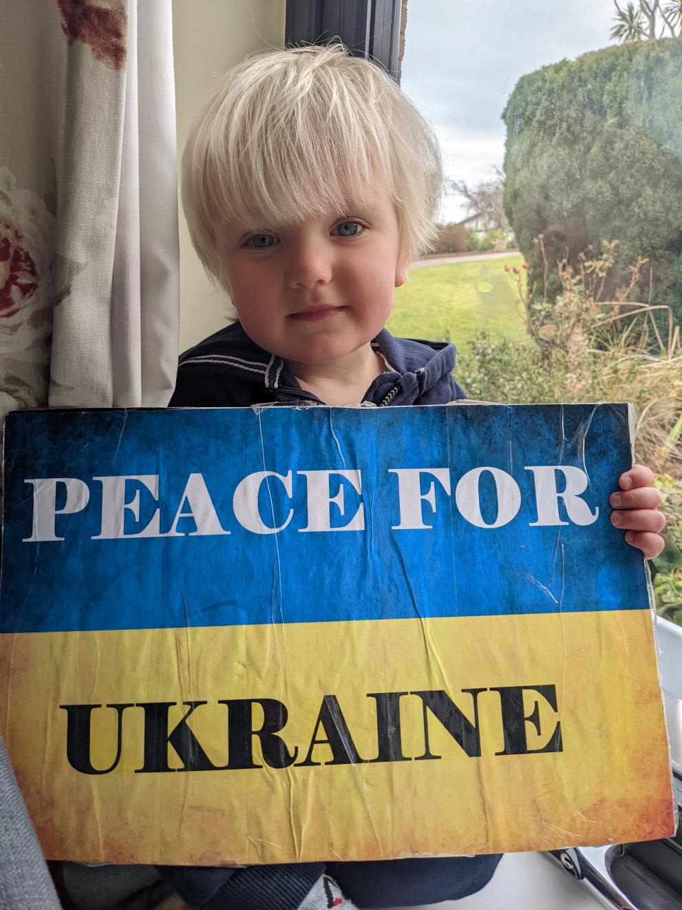 A 2 year-old Irish girl with Ukrainian roots, holding a protest poster that says "Peace for Ukraine".